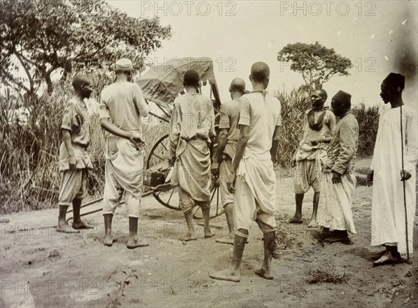 Broken rickshaw, Uganda. A group of African servants consider what to do with rickshaw that has broken down on a country track. Uganda, 1906. Uganda, Eastern Africa, Africa.