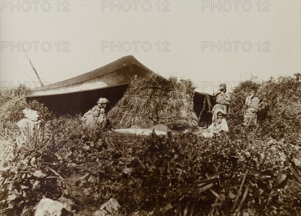 Temporary dwelling, Morocco. A group of people sit around a harvested bundle of straw outside a temporary canvas dwelling in the countryside. Morocco, 1898. Morocco, Northern Africa, Africa.