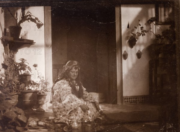 Mrs Russi dressed as a 'moorish woman'. Mrs Russi, a European woman, sits in the doorway of a colonial house dressed up as a 'moorish woman'. Clothed in a robe, she wears her hair (or wig) long and loose. Safi, Morocco, 1898. Safi, Safi, Morocco, Northern Africa, Africa.