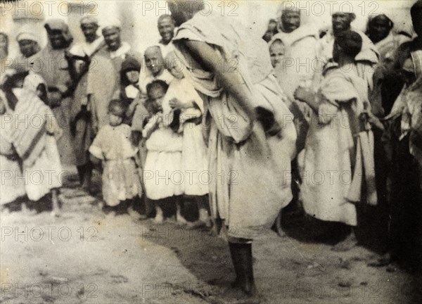 Storytelling at Safi. A 'halaiqui' (storyteller) hops on one leg as he entertains a 'halca' (audience) with traditional tales in the market place at Safi. Safi, Morocco, 1898. Safi, Safi, Morocco, Northern Africa, Africa.