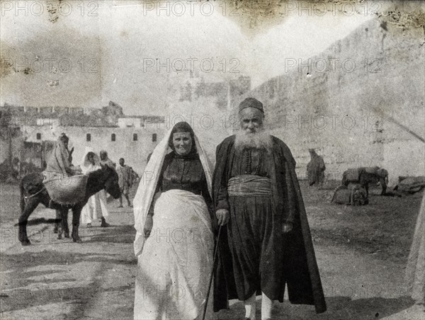 A Jewish couple in Morocco. Portrait of a middle-aged Jewish couple wearing traditional dress. The woman wears a high-buttoned shirt, wrap-around skirt and headscarf: her husband, a cape and cummerbund. Safi, Morocco, 1898. Safi, Safi, Morocco, Northern Africa, Africa.
