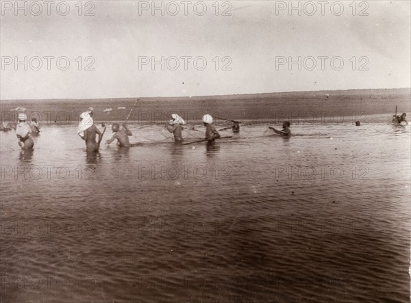 Moroccan men fishing. A group of Moroccan men, naked and up to their waists in water, hold fishing nets stretched out between them as they walk through a shallow lake. Southern Morocco, 1898. Morocco, Northern Africa, Africa.