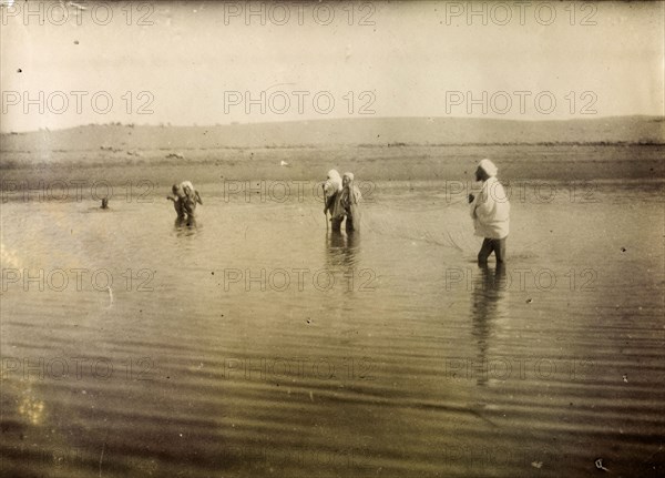 Fishing in south Morocco. A group of Moroccan men stand up to their knees in water, holding a fishing net stretched out between them in the middle of a shallow lake. Southern Morocco, 1898. Morocco, Northern Africa, Africa.