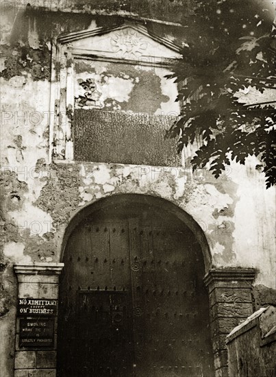 Entrance to the fort. A closed wooden doorway forms the entrance to a fortifed complex identified only as 'the fort'. A sign to the left of the door reads: 'NO ADMITTANCE EXCEPT ON BUSINESS'. Probably Kenya, 1906., Eastern Africa, Africa.