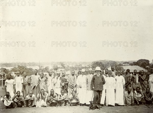 Tsetse fly researchers. A European official poses with Africans in a variety of costumes. A caption says they are 'in search of tsetse fly', suggesting that they were part of the colonial administration's attempt in the early twentieth century to map the distribution of tsetse fly in British East Africa. British East Africa (Kenya), 1906. Kenya, Eastern Africa, Africa.