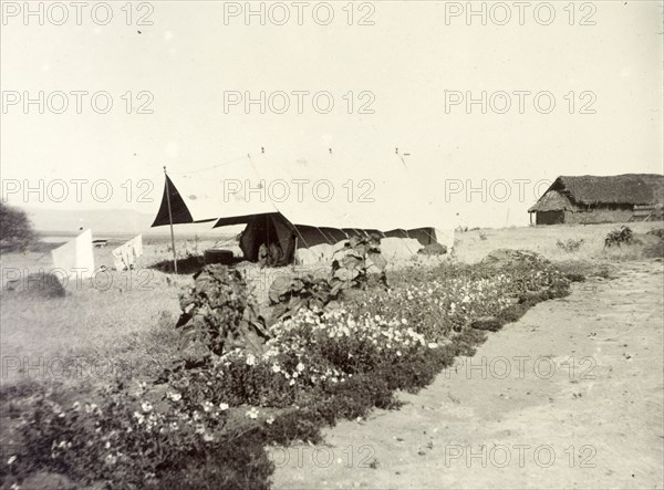 Frederick Stanbury's tent. Frederick Stanbury's tent, pitched by a roadside near to a large thatched roof building. British East Africa (Kenya), 1906. Kenya, Eastern Africa, Africa.