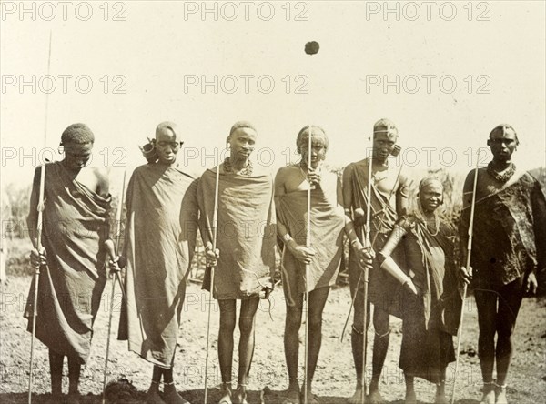 Maasai youths. A group of Maasai youths line up for the camera wearing traditional dress and holding staffs. British East Africa (Kenya), 1906. Kenya, Eastern Africa, Africa.
