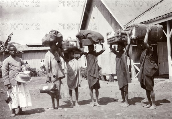 Porters at the station. Frederick Stanbury's safari porters balance large bundles of luggage on their heads as they wait at a railway station. Nairobi, British East Africa (Kenya), 1906. Nairobi, Nairobi Area, Kenya, Eastern Africa, Africa.
