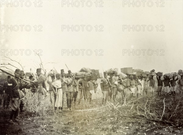 Frederick Stanbury's porters. Frederick Stanbury's porters and servants wait in line holding various items of luggage on a hunting safari to Lake Baringo. British East Africa (Kenya), 1906. Kenya, Eastern Africa, Africa.