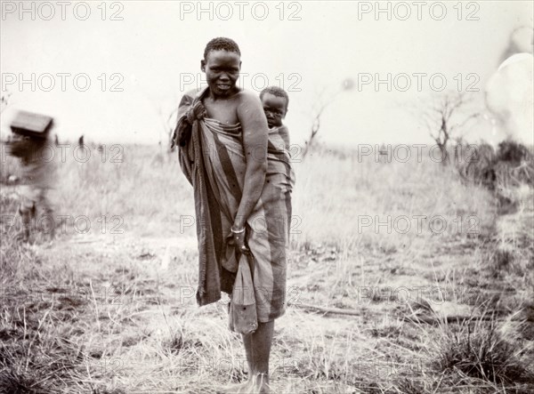 Kenyan woman and child. Portrait of a Kenyan woman, her baby strapped to her back with a length of wrap-around cloth. British East Africa (Kenya), 1906. Kenya, Eastern Africa, Africa.
