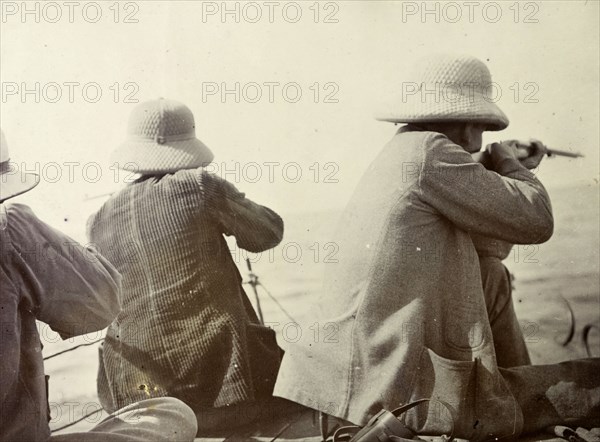 Shooting hippopotamus on Lake Victoria. A back view of three European men aiming at hippopotami (invisible in the image) from the deck of boat on Lake Victoria. British East Africa (Kenya), 1906., Rift Valley, Kenya, Eastern Africa, Africa.