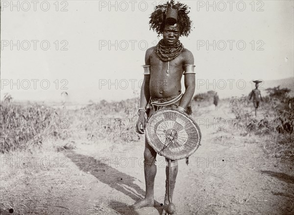 Medicine man, Kenya. Full-length portrait of a man identified in the original caption as a 'witch doctor'. Wearing a headdress and a heavily beaded necklace, he stands proudly holding a wickerwork shield. Near Lake Victoria, British East Africa (Kenya), 1906., Nyanza, Kenya, Eastern Africa, Africa.