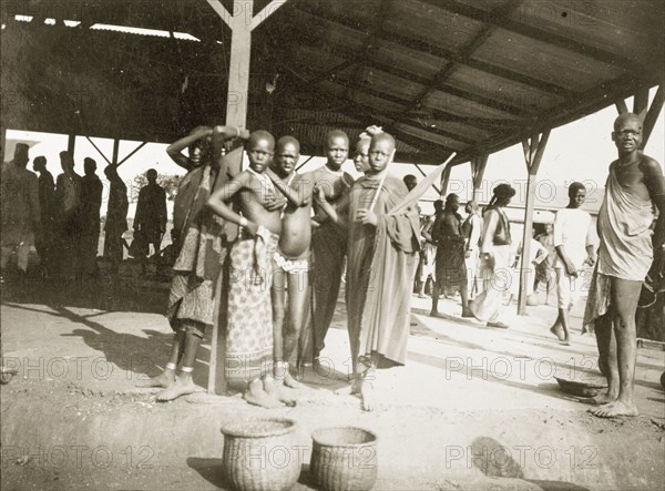Grain traders in the market at Kisumu. African men and women stand beneath a modern market canopy: grain baskets in front of them. Kisumu, British East Africa (Kenya), 1906. Kisumu, Nyanza, Kenya, Eastern Africa, Africa.