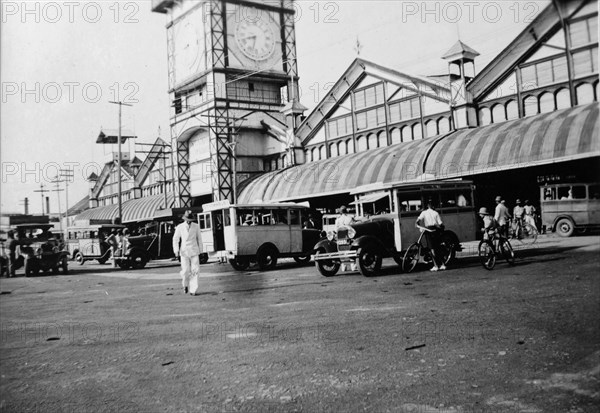 Buses outside the market. Buses parked outside the large clock tower in the central market place. Janjanbureh, Gambia, circa 1935. Janjanbureh, Central River, Gambia, Western Africa, Africa.
