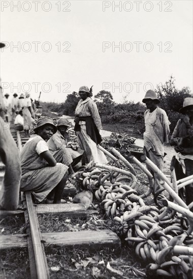 Banana sellers, Uganda. Banana sellers hope to attract passing trade beside a railway track and river. Uganda, circa 1935. Uganda, Eastern Africa, Africa.