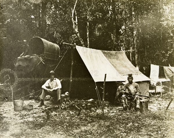 British survey camp. Trigonometrical survey camp of a British surveyor and his Malayan assistant. An elephant used as transport for the trip can be seen in the background. Probably in upper Perak, British Malaya (Malaysia), circa 1901., Perak, Malaysia, South East Asia, Asia.