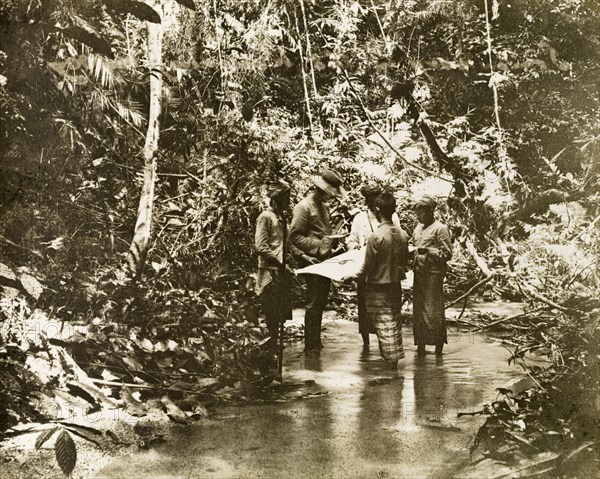 Surveying in the Kenering Valley.. A European surveyor and his Malay assistants, part of a British-led trigonometrical survey team, consult a chart in the Kenering valley. Perak, British Malaya (Malaysia), circa 1902., Perak, Malaysia, South East Asia, Asia.