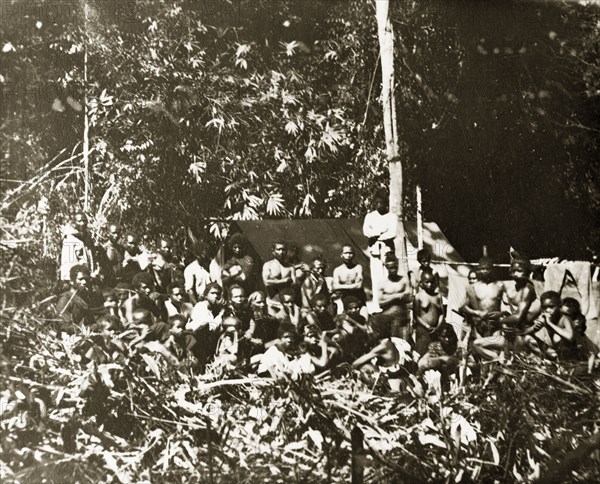 Paying hired Malaysian tribal guides. A large group of Malaysian aborigines (Orang Asli) wait for payment at a camp following a trip to Gerah that they have undertaken as hired guides and porters. Near Gerah, British Malaya (Malaysia), 1905. Gerah, Perak, Malaysia, South East Asia, Asia.