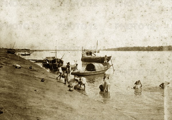 Washing in the River Ganges. People wash themselves in the River Ganges beside several small fishing boats moored off a sandbank. Chandernagore, India, 1890. Chandernagore, West Bengal, India, Southern Asia, Asia.