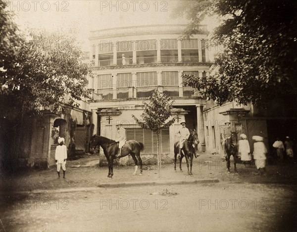 Saddling up outside a colonial house. S.A.H. Sitwell and friends pose on horseback in the walled compound of a multi-storeyed colonial house with wide verandas and blinds. Several Indian servants are also present. Calcutta (Kolkata), India, August 1895. Kolkata, West Bengal, India, Southern Asia, Asia.