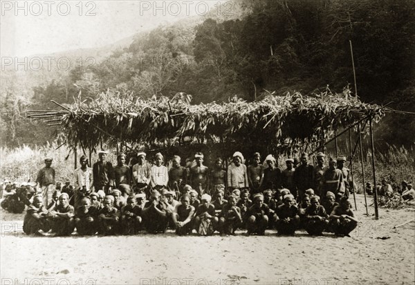 Chin tribesmen, Burma (Myanmar). Group portrait of Chin tribesmen from the Chin Hills. Several dozen men squat or stand in a sandy clearing beneath a makeshift, grass-roofed shelter. Other people, possibly Chin women, are seated at a distance. Rakhine, Burma (Myanmar), January 1897., Rakhine, Burma (Myanmar), South East Asia, Asia.