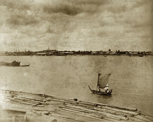 A sailing boat at Rangoon. A small sailing boat navigates rafts of teak timbers floating on a wide river. Rangoon (Yangon), Burma (Myanmar), circa 1885. Yangon, Yangon, Burma (Myanmar), South East Asia, Asia.