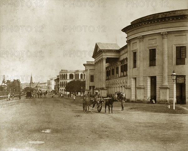 Strand Road in Rangoon. Pedestrians and cattle-drawn carts meander along Strand Road. Rangoon (Yangon), Burma (Myanmar), circa 1885. Yangon, Yangon, Burma (Myanmar), South East Asia, Asia.