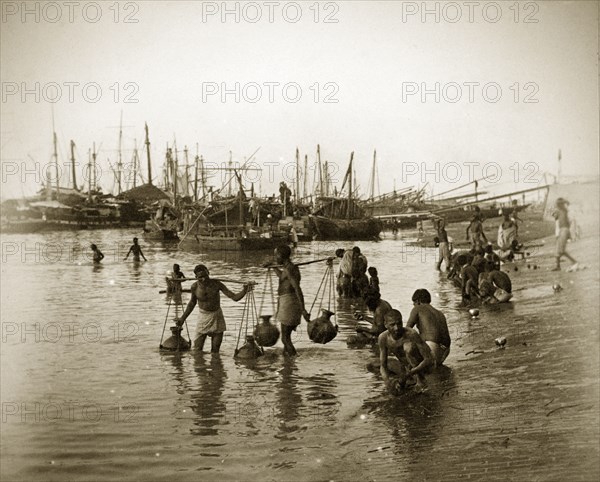 Calcutta water carriers. Water carriers fill their pitchers on the banks of the Hooghly River. The masts and booms of numerous sailing ships punctuate the skyline behind them. Calcutta (Kolkata), India, circa 1890. Kolkata, West Bengal, India, Southern Asia, Asia.