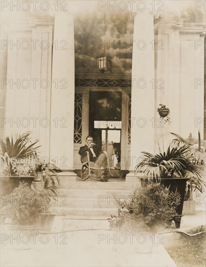 Archie Cooper reclines in a rocking chair. Archie Cooper, Chief Executive Officer of the Peruvian Corporation, reclines in a rocking chair on the grand, pillared porch at the entrance to his house. Lima, Peru, 1920. Lima, Lima Metropolitana, Peru, South America, South America .