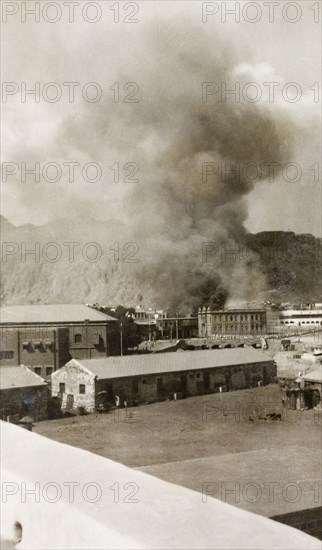 Riot damage in Aden, 1947. A large plume of smoke billows from a building in the Jewish quarter of Aden, during the Arab riots that took place between 1-3 December 1947 in response to the United Nations Partition Plan for Palestine. Aden, Yemen, December 1947. Aden, Adan, Yemen, Middle East, Asia.