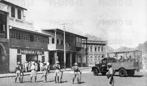 Armed police during the Arab riots in Aden, 1947. Armed police climb out of an armoured vehicle and assemble on a street in Aden, where a group of people are sheltering in the doorway of the Exchange Bank of India and Africa Ltd building, during the Arab riots that took place between 1-3 December 1947 in response to the United Nations Partition Plan for Palestine. Aden, Yemen, December 1947. Aden, Adan, Yemen, Middle East, Asia.