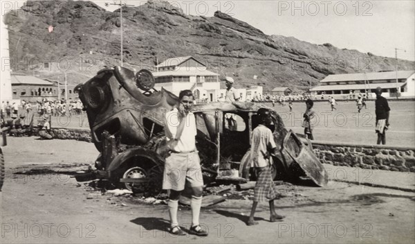 Vehicles destroyed during Arab riots in Aden, 1947. A European man stands by the burnt out shells of two upturned cars near a recreation ground in Aden, after the Arab riots that took place between 1-3 December 1947 in response to the United Nations Partition Plan for Palestine. Aden, Yemen, December 1947. Aden, Adan, Yemen, Middle East, Asia.