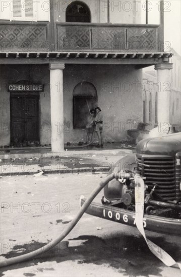 Fire fighters in Aden during the Arab riots, 1947. Two fire fighters extinguish a fire in 'Cohen Store' in Aden from a hose pipe attached to a tap on the front of a fire engine, during the Arab riots that took place between 1-3 December 1947 in response to the United Nations Partition Plan for Palestine. Aden, Yemen, December 1947. Aden, Adan, Yemen, Middle East, Asia.
