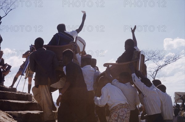 Kenneth Kaunda arriving at United National Independence Party rally. Kenneth Kaunda (born 1924), President of UNIP, and Munukayumbwa Sipalo, Secretary-General of UNIP, are carried in wicker chairs to the podium to address a crowd of supporters at a UNIP political rally. Kitwe, Northern Rhodesia (Zambia), circa 1962. Nkana-Kitwe, Copperbelt, Zambia, Southern Africa, Africa.