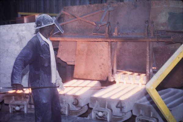 Moulding copper, Nkana-Kitwe. A smith oversees the pouring of refined copper from a furnace into moulds at a copper factory. Nkana-Kitwe, Northern Rhodesia (Zambia), circa 1962. Nkana-Kitwe, Copperbelt, Zambia, Southern Africa, Africa.