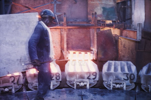Moulding copper, Nkana-Kitwe. A smith oversees the pouring of refined copper from a furnace into moulds on a conveyor belt at a copper factory. Kitwe, Northern Rhodesia (Zambia), circa 1962. Nkana-Kitwe, Copperbelt, Zambia, Southern Africa, Africa.