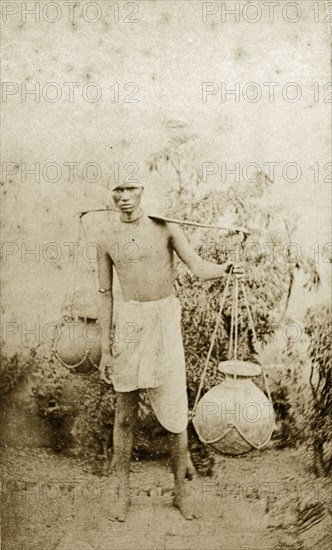 Indian water carrier. Portrait of an Indian man transporting water in clay pots tied to either end of a long pole carried over his shoulder. India, circa 1890. India, Southern Asia, Asia.