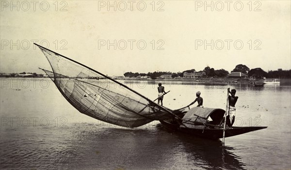 Fishing with a large net, India. Two fishermen steady a small boat with long poles for another who lowers a large net into the river. India, circa 1890. India, Southern Asia, Asia.