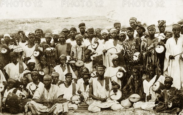 Tom-tom drummers. A group of dancers and tom-tom drummers pose for the camera holding curved drumsticks poised over their instruments. Nigeria, circa 1928. Nigeria, Western Africa, Africa.
