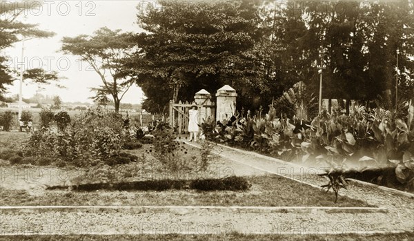 Lagos Club gardens. A European woman in a dress and sun hat stands on a pathway at the entrance to the Lagos Club gardens. Nigeria, 1928. Lagos, Lagos, Nigeria, Western Africa, Africa.