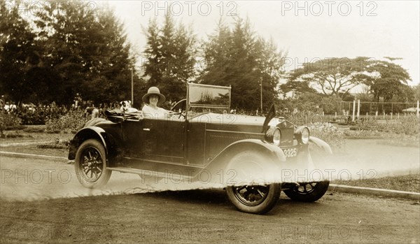 Driving in the grounds. A European woman poses for the camera from an open-topped car in the grounds of the Lagos Club. A small dog travels as her companion in the rear seat. Lagos, Nigeria, 1928. Lagos, Lagos, Nigeria, Western Africa, Africa.