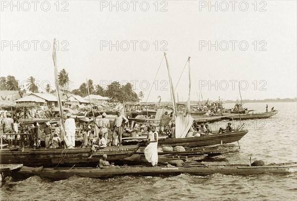 Market day in Badagry. People aboard fishing boats crowd the waterside at Badagry harbour on market day. Badagry, Nigeria, circa 1925. Badagry, Lagos, Nigeria, Western Africa, Africa.