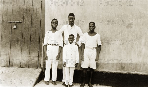 Domestic servants of Mrs Flack. Domestic servants of Mrs Flack pose for the camera against a wall. The three young African men and a boy, 'Edward', are all barefoot and dressed in white. Badagry, Nigeria, circa 1928. Badagry, Lagos, Nigeria, Western Africa, Africa.