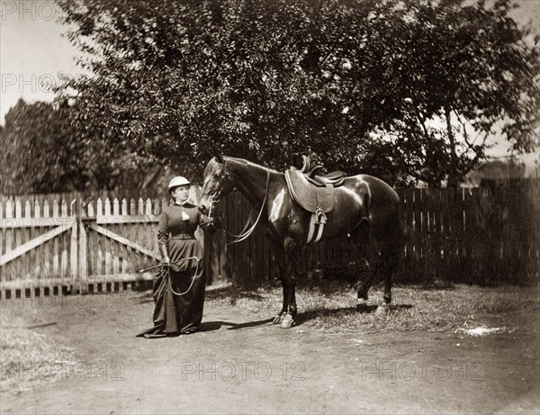 Woman and horse, Australia. A woman dressed in riding habit and helmet holds a horse by the reins in a fenced paddock or garden. The horse has been saddled with a side saddle. Queensland, Australia, circa 1890., Queensland, Australia, Australia, Oceania.