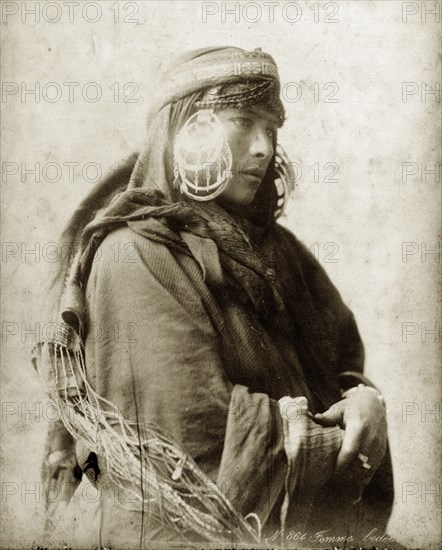 Portrait of a bedouin woman. Portrait of a north African bedouin woman. She wears large, striking earrings that catch the light, and braids in her hair that peep out from under her tassled headscarf. North Africa, circa 1885., Northern Africa, Africa.