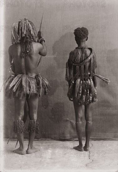 Andaman Islanders. A man and a woman from the Andaman Islands stand, backs facing the camera, against an unpainted backdrop. The man holds a bow and long arrows: both wear grass-like aprons and neckpieces. Andaman Islands, India, circa 1900., Andaman and Nicobar Islands, India, Southern Asia, Asia.