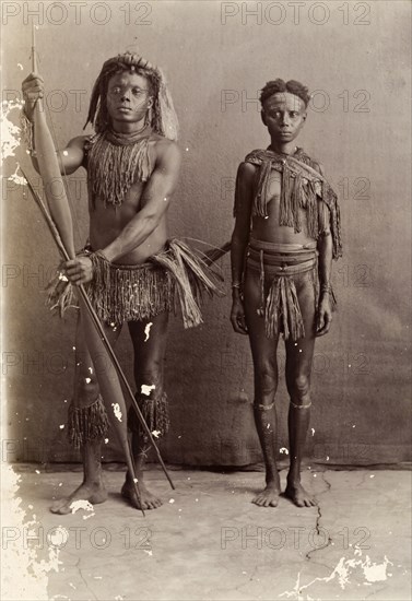 Couple from the Andaman Islands. A man and a woman from the Andaman Islands stand, facing the camera, against an unpainted backdrop. The man holds a bow and long arrows: both wear grass-like aprons and neckpieces. Andaman Islands, India, circa 1900., Andaman and Nicobar Islands, India, Southern Asia, Asia.