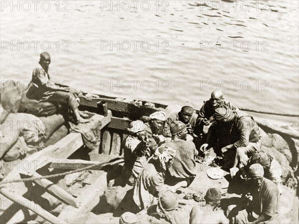 Coal workers at lunch. Several coal porters sit aboard an open wooden barge as they eat their lunch. Persian Gulf, circa 1900., Middle East, Asia.