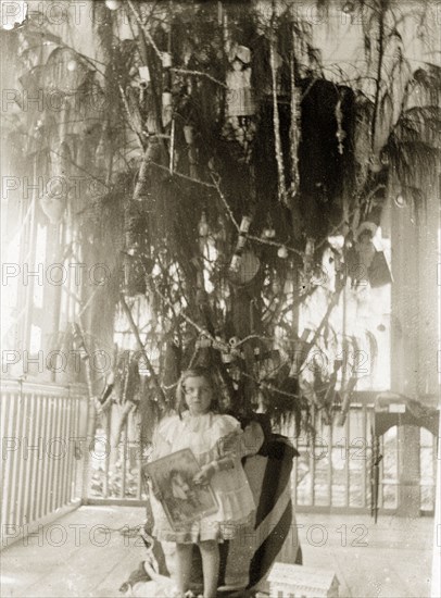 Marjory's Christmas Tree'. A young girl identified as 'Marjory' poses for the camera in front of an exotic plant adorned with traditonally Western Christmas decorations including tinsel and crackers. Anadaman Islands, India, circa 1908., Andaman and Nicobar Islands, India, Southern Asia, Asia.