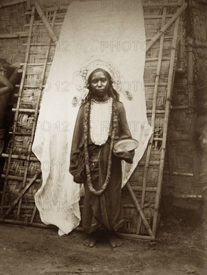Young mendicant girl. A young female mendicant stands, bowl in hand, dressed in a headdress, a garland strung around her neck. Probably north India, circa 1890. India, Southern Asia, Asia.